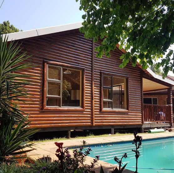 Log cabin beside a swimming pool and leafy tree